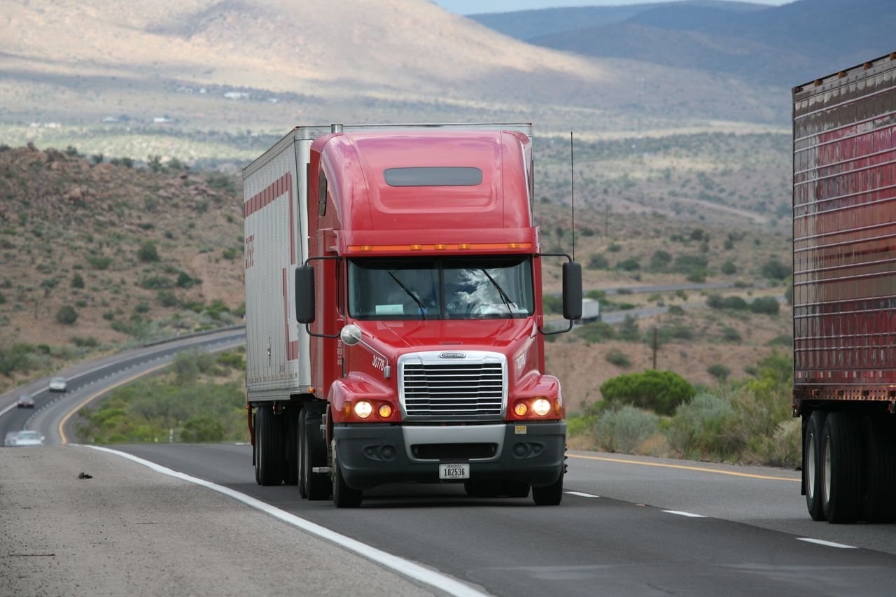 Free Red semi-truck driving through scenic highway in a mountainous landscape. Stock Photo
