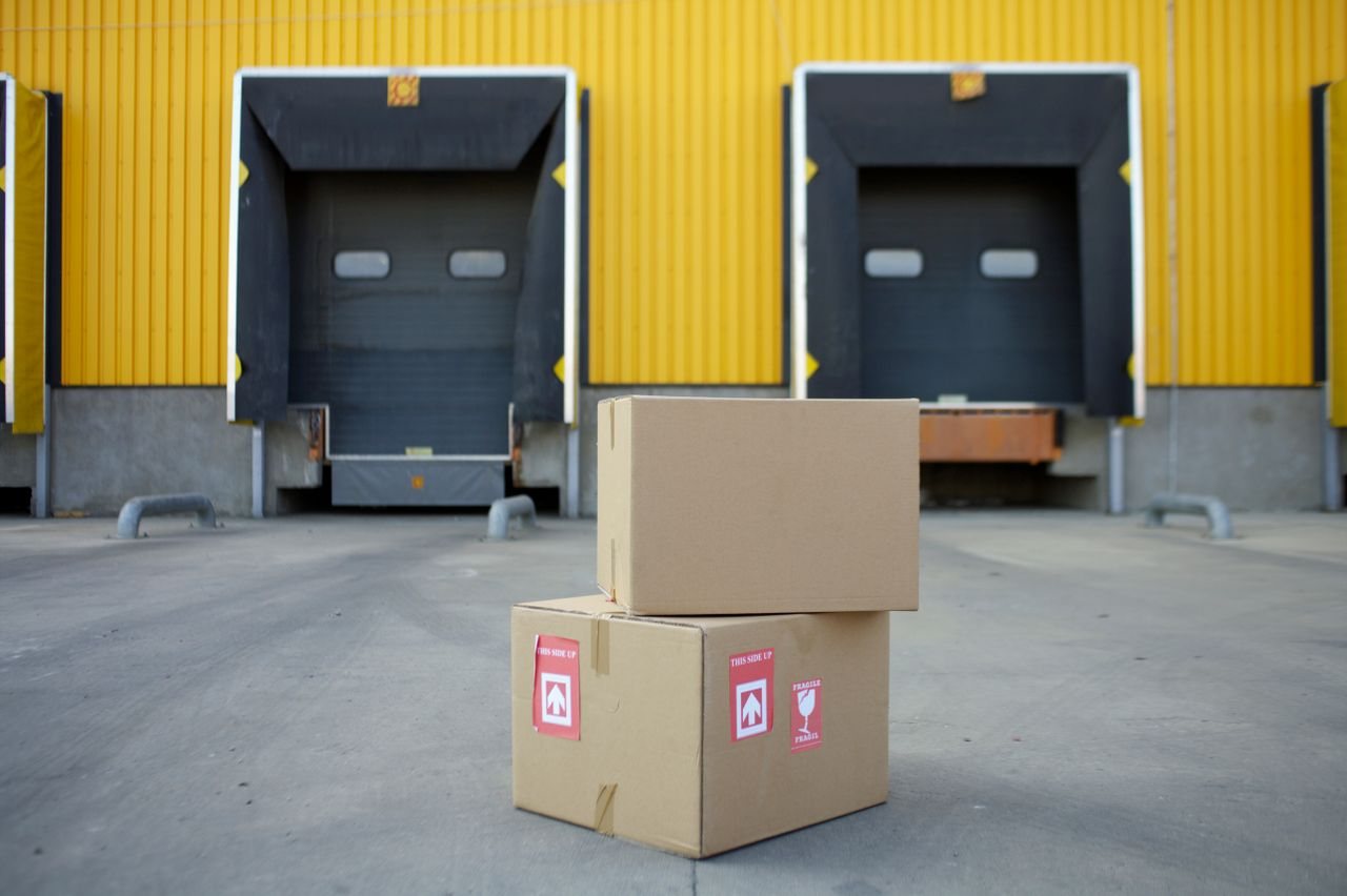 Free Cardboard boxes stacked in front of industrial warehouse loading docks with yellow walls. Stock Photo